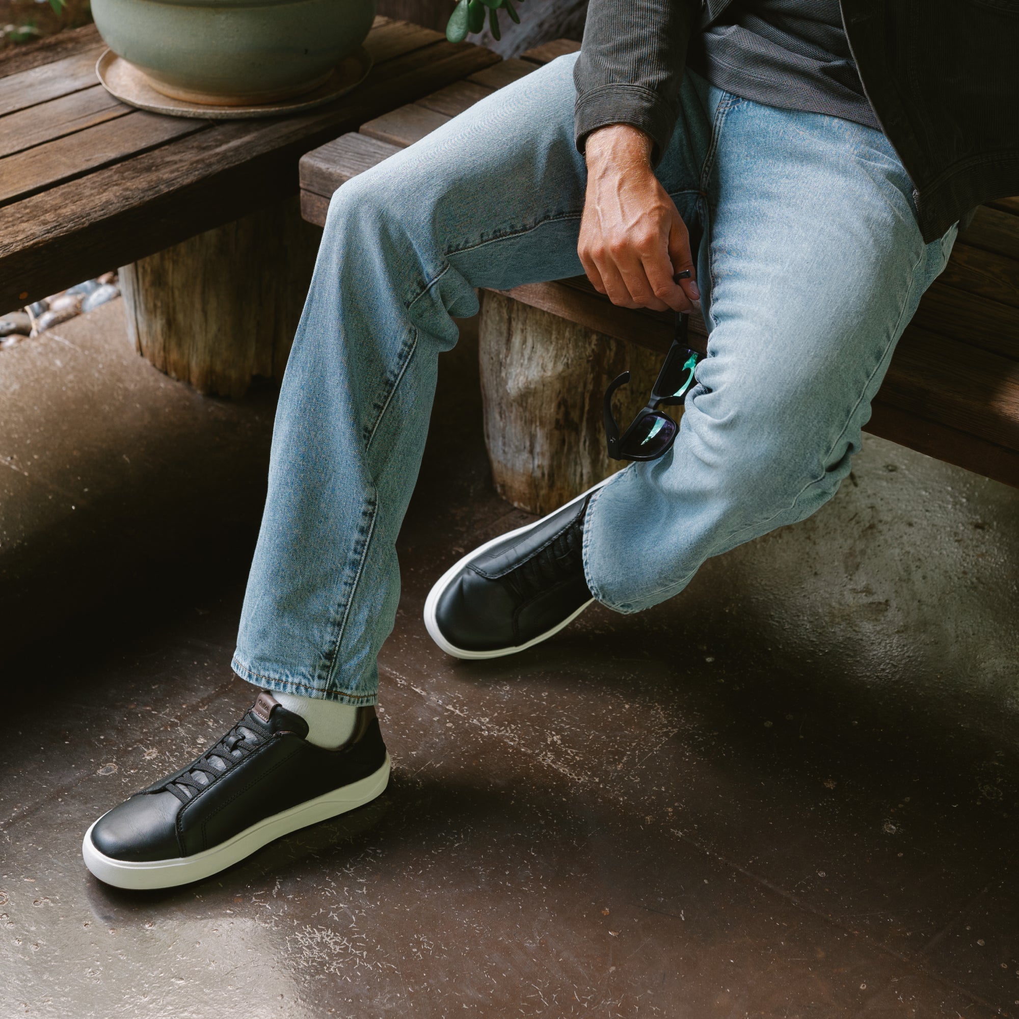 Person wearing black leather sneakers with white sole and laces, styled with light blue jeans.